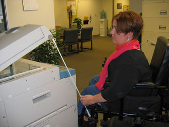 A wheelchair rider to raises the lid of a copy machine with a push rod.